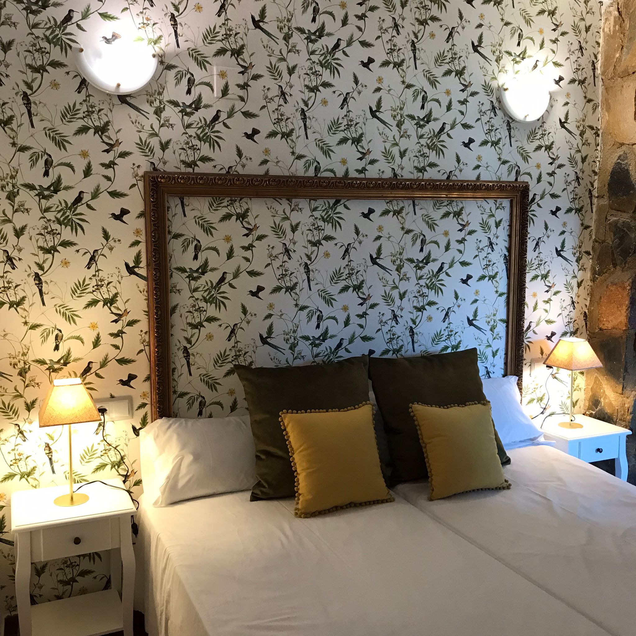 Un dormitorio con una cama grande, dos mesitas de noche, una lámpara de pared y un espejo decorativo.