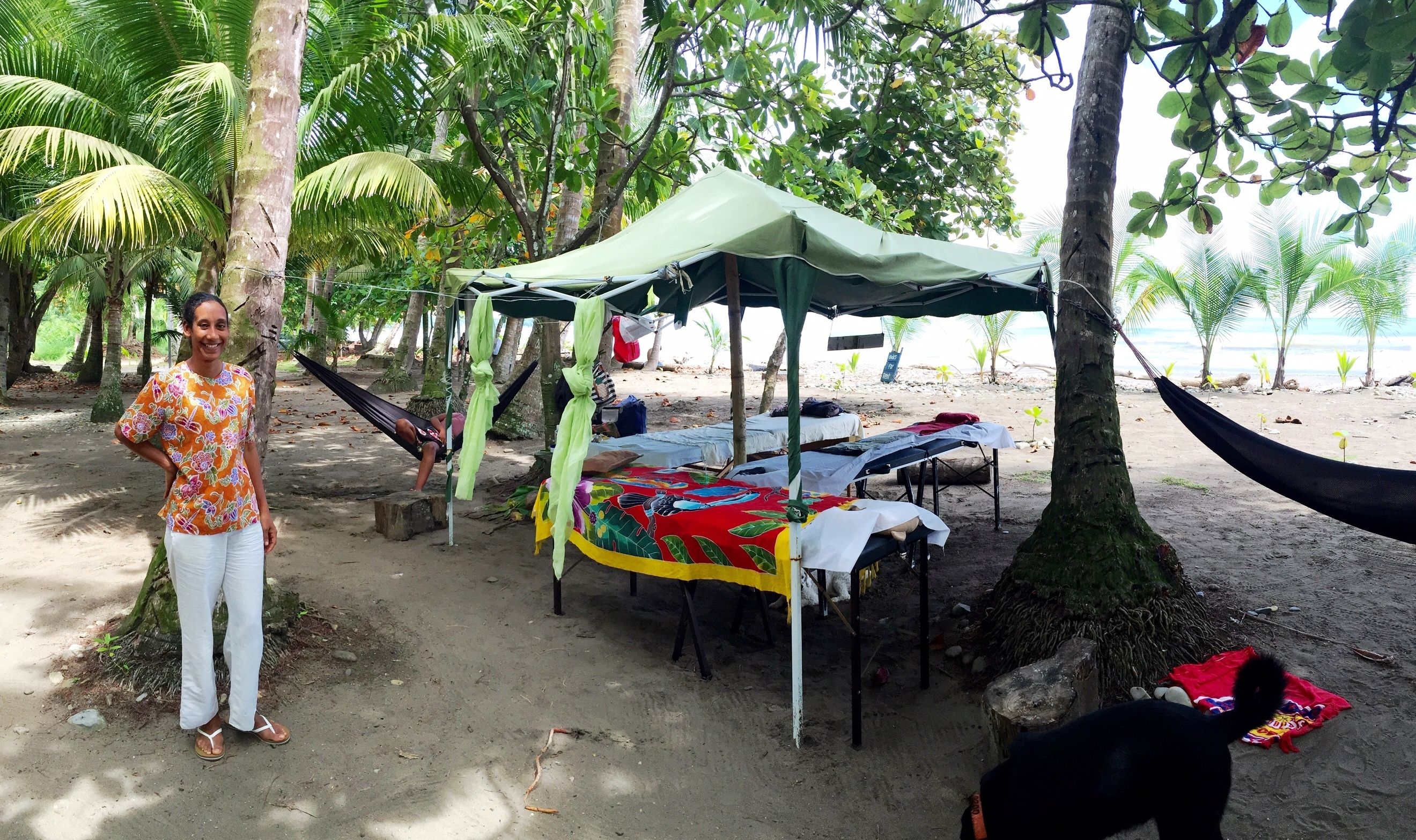 A beachside setup with a hammock, a table with a colorful tablecloth, and a tent.