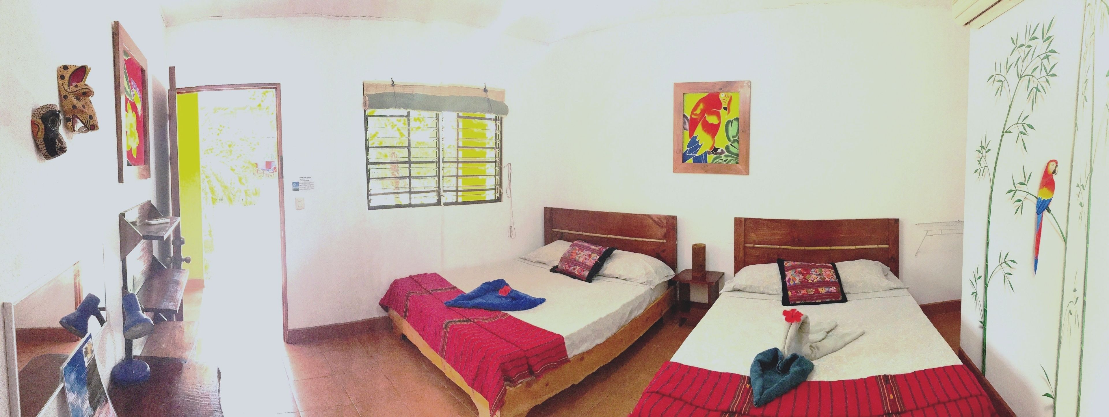 A room with two beds, a window with bars, a wooden headboard, and a wall with a colorful painting.