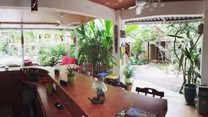 A dining area with a long wooden table, chairs, and potted plants. - Tropical Sands Dominical Eco Inn (Bahía Ballena)
