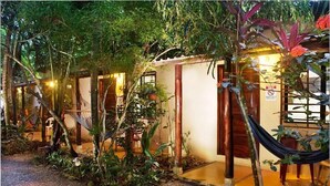 A row of small, single-story buildings with wooden doors and a garden area in front. - Tropical Sands Dominical Eco Inn (Bahía Ballena)