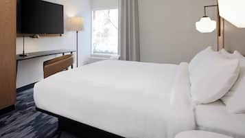 A hotel room with a large bed, a desk with a chair, a flat-screen TV mounted on the wall, and a window with curtains.