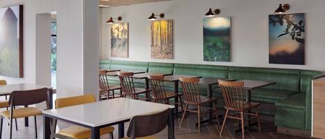 A restaurant with wooden tables and chairs, a green cushioned bench, and wall-mounted artwork.