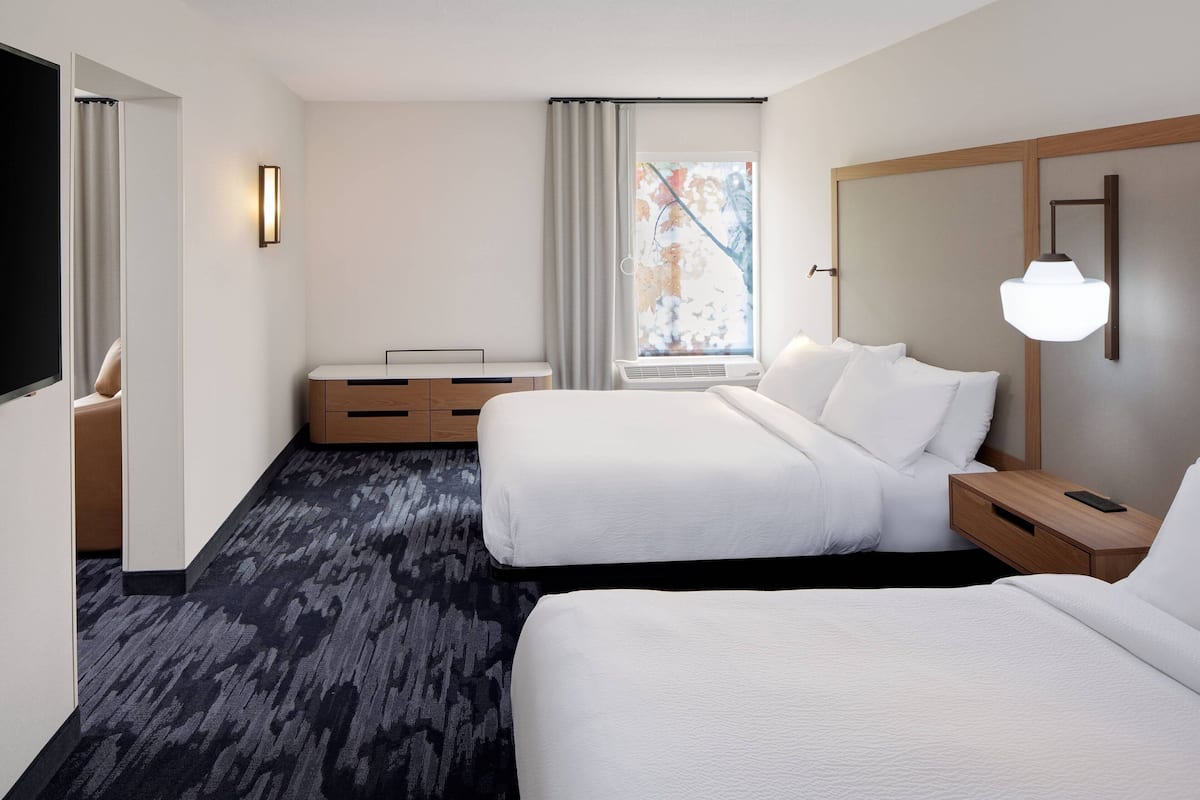 Habitación de hotel con dos camas, un escritorio, una silla, una ventana con cortinas y una lámpara fijada a la pared.