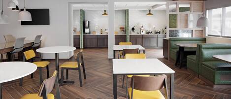 A modern dining area with round tables and yellow chairs, a kitchen in the background, and a green booth seating area.