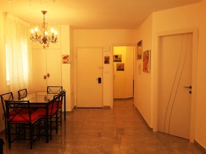 A dining area with a glass table and chairs, a chandelier, and a door leading to another room.
