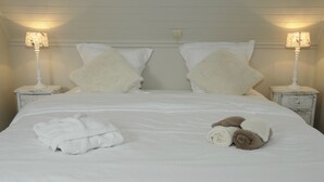 A neatly made bed with white linens and two pillows, two bedside lamps, and a rolled towel on the bed. - Guesthouse La Cereza (Brakel)