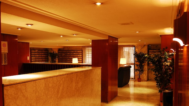 A hotel reception area with a marble counter, a reception desk, and a seating area with a plant. - Apartamentos Goya 75 (Madrid)
