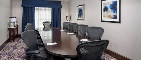A conference room with a long table, multiple chairs, a coffee station, and two framed floral paintings on the walls.
