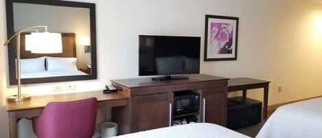 Une chambre d’hôtel équipée d’un lit, d’un bureau avec un ordinateur, d’une télévision, d’un four à micro-ondes et d’une poubelle.
