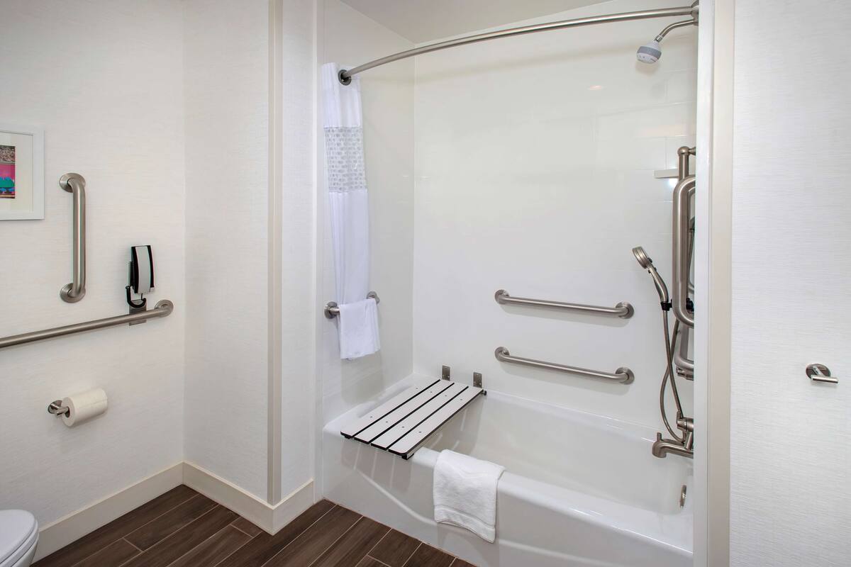 A modern bathroom with a walk-in shower, grab bars, a towel rack, and a toilet paper holder.