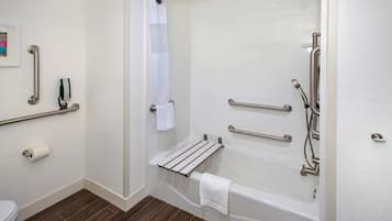 Un baño moderno con ducha a ras de suelo, barras de apoyo, un perchero para toallas y un sujetabrazos de papel higiénico.