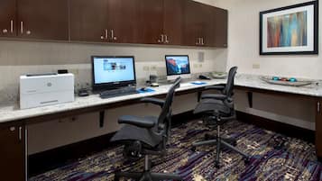A hotel office with two desks, computers, chairs, and a carpeted floor.