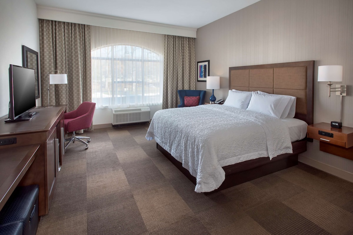 A hotel room with a large bed, a desk with a computer, a chair, and a TV.