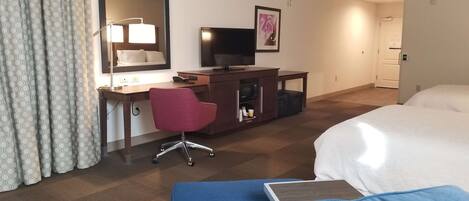 Habitación de hotel con cama, escritorio con computadora, silla, televisión y puerta de baño.