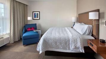 A hotel room with a large bed, a blue armchair, a small table, and a wall-mounted lamp.