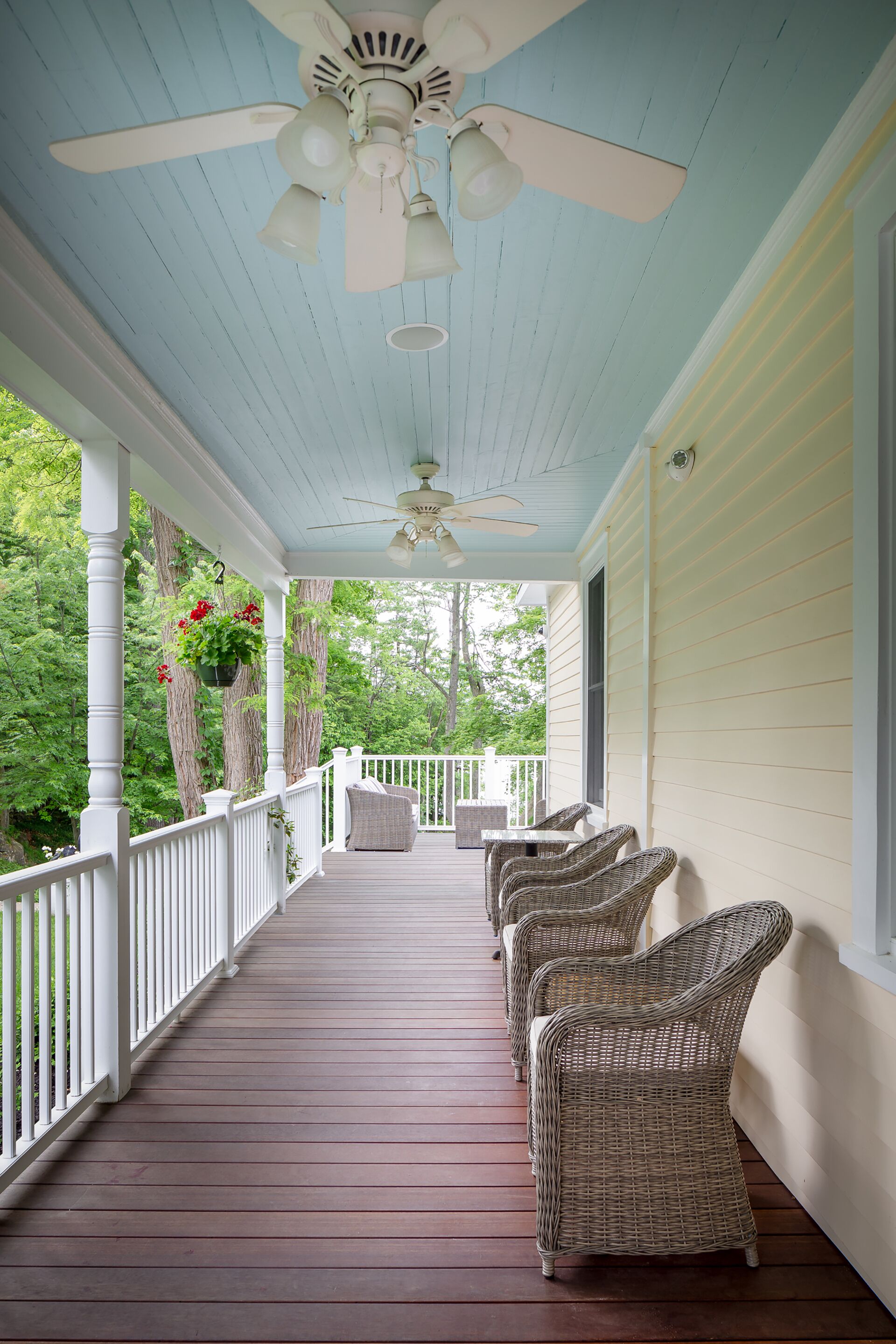 A covered porch with wicker furniture, a ceiling fan, and hanging flower baskets.