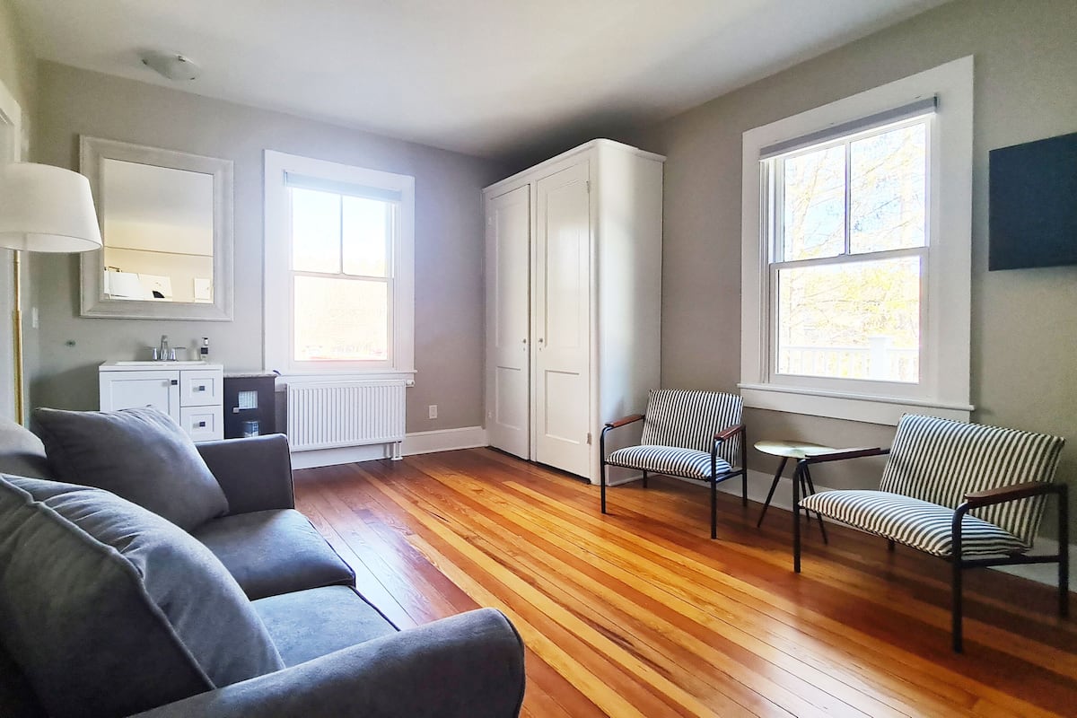A modern living room with a grey sofa, striped chairs, a small table, and large windows.