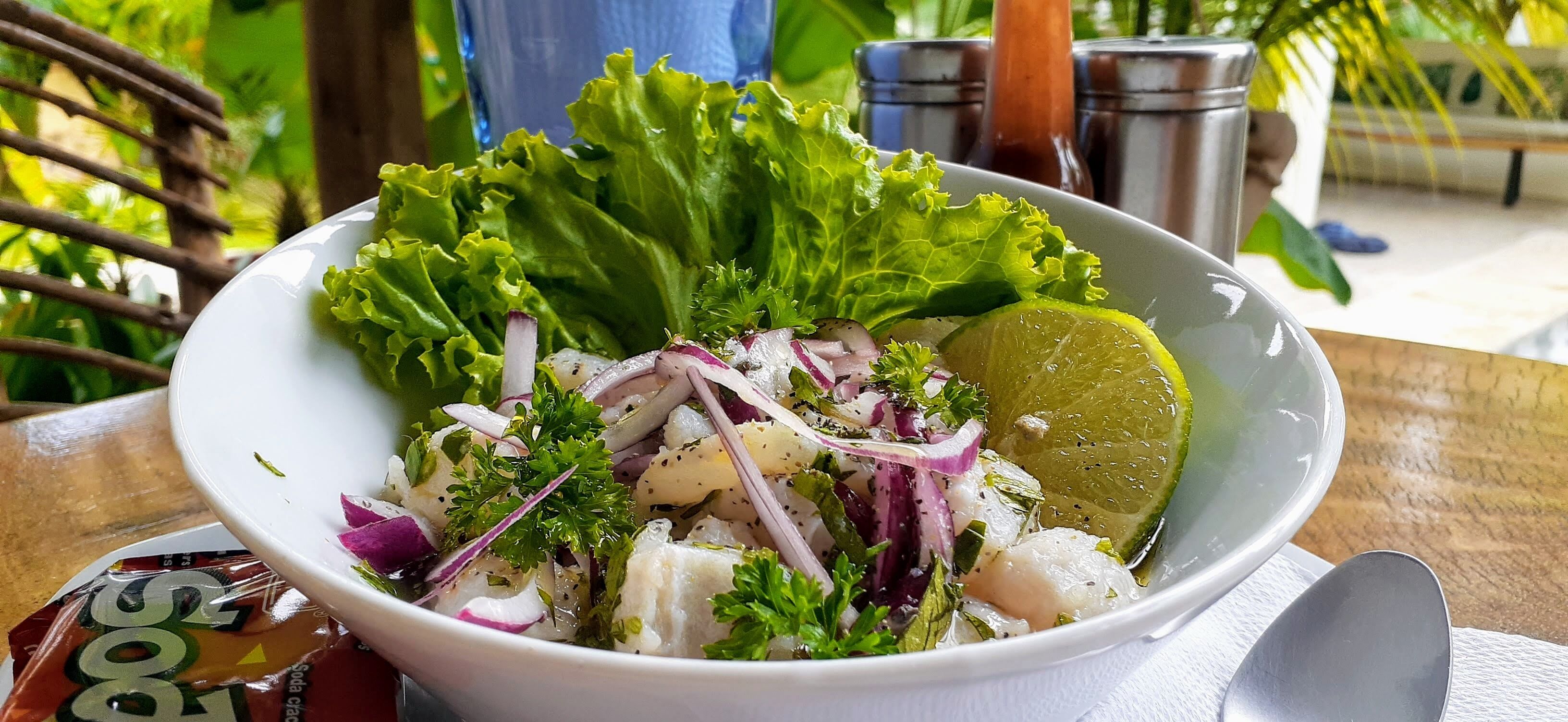Un tazón de ensalada de mariscos con lechuga, cebollas rojas y lima sobre una mesa de madera.