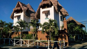 A resort with thatched-roof buildings, palm trees, and a fenced area. - Nayal Lodge (León)