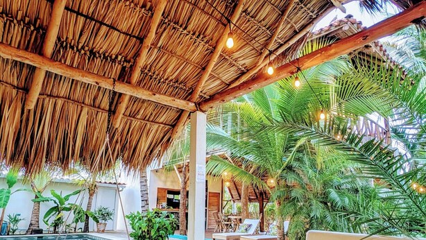 A poolside area with a thatched roof, lounge chairs, and a hammock. - Nayal Lodge (León)