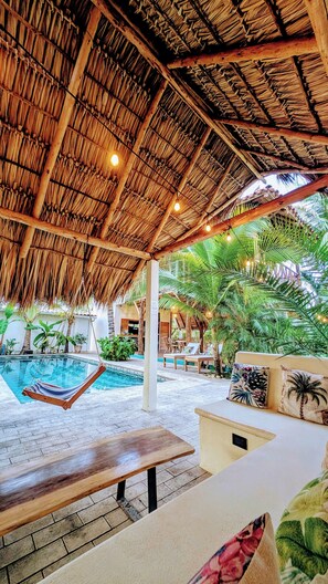 Un espace aménagé au bord de la piscine, doté d’un toit de chaume, de chaises longues et d’un hamac.