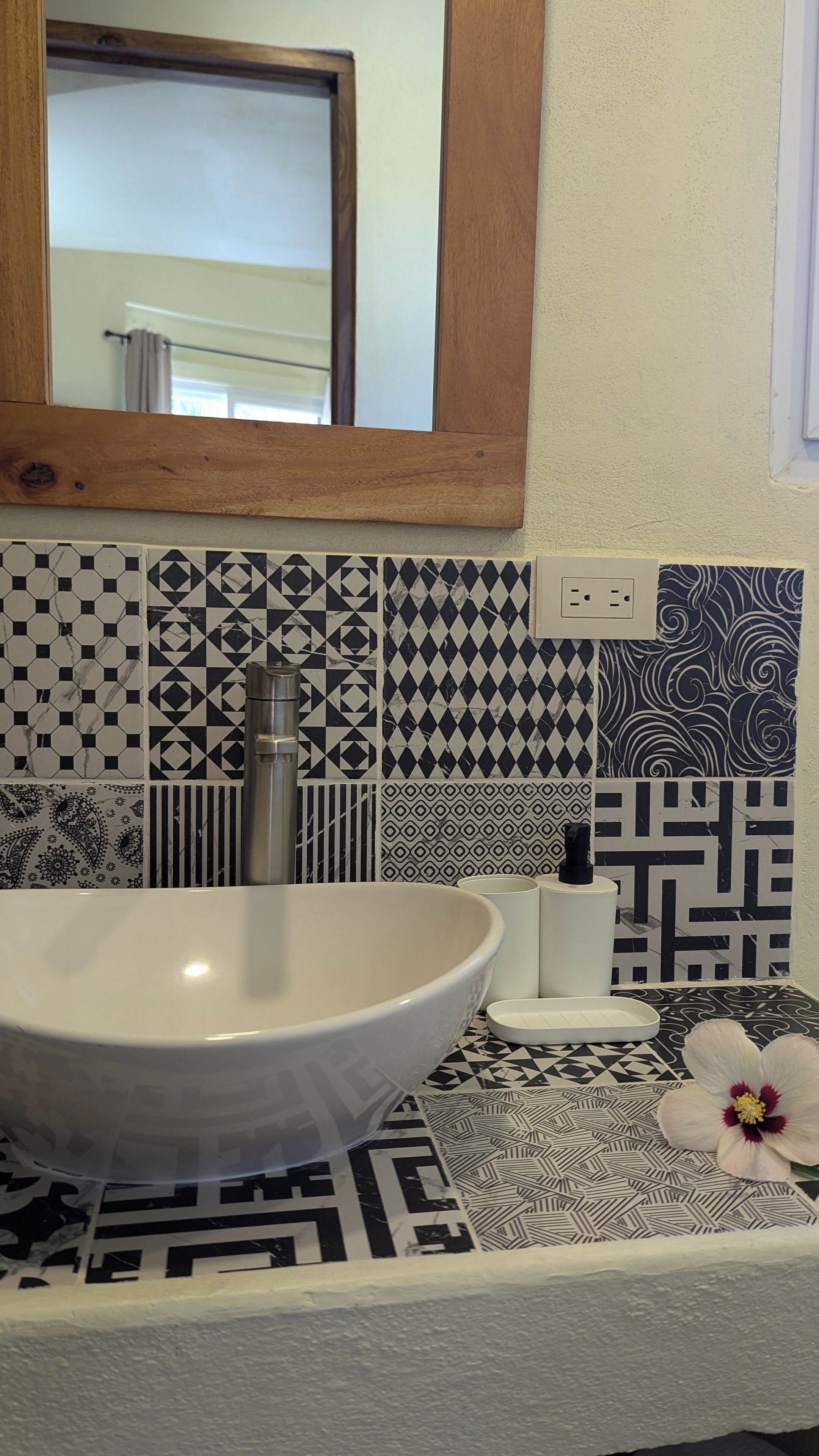 Une salle de bain avec un lavabo blanc, un miroir et des carreaux à motifs.