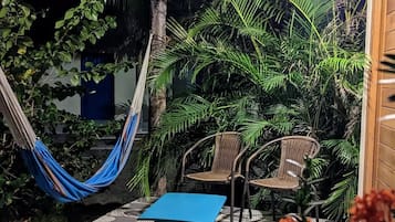 Un área de estar al aire libre con techo de paja, sillas de mimbre y una mesa azul.