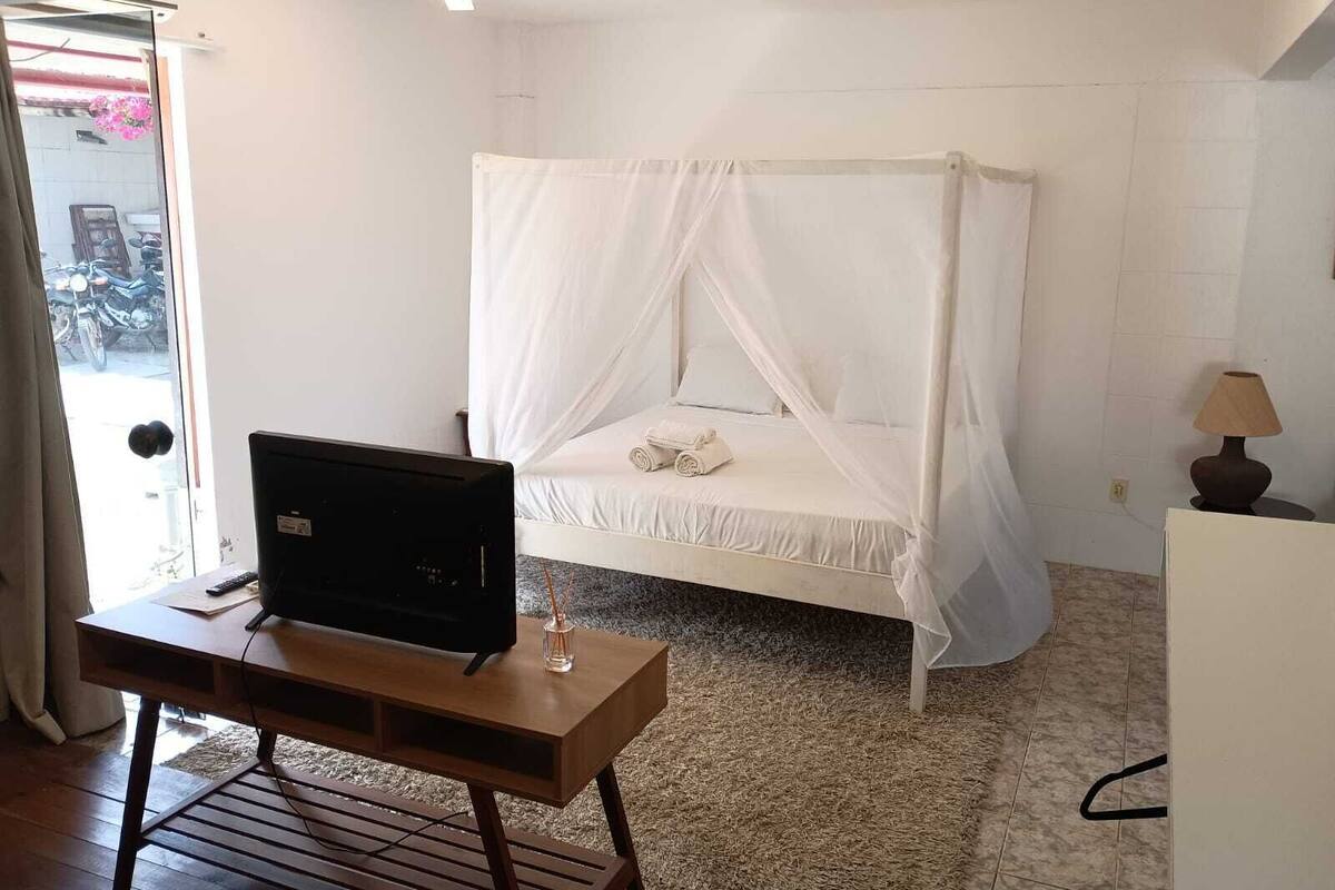 Une chambre à coucher avec un lit, un téléviseur posé sur une table en bois et une lampe.