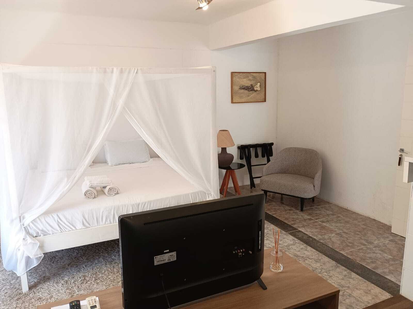 A bedroom with a bed, a TV, a chair, and a desk.