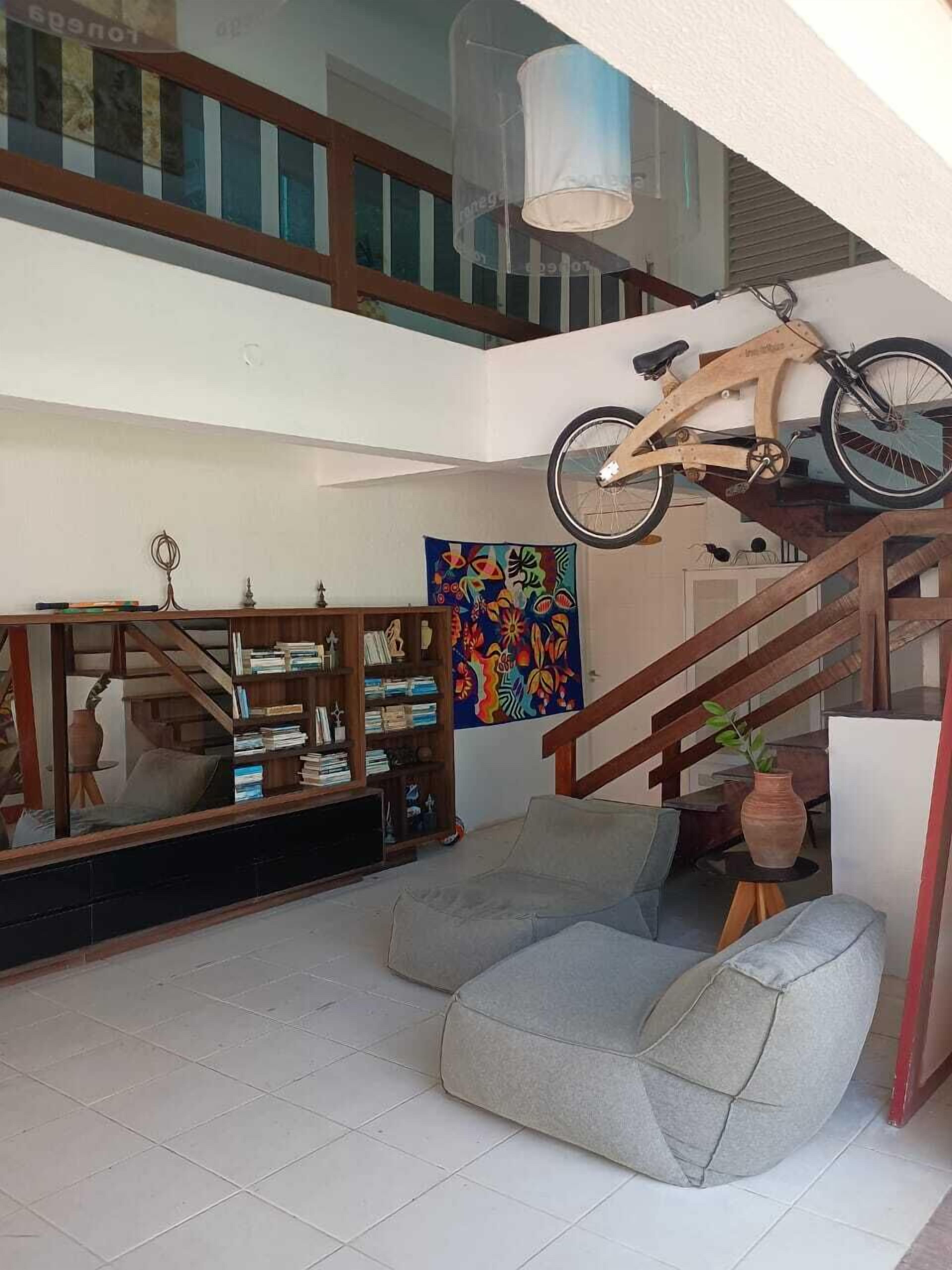 A spacious living area with a staircase, a wooden bookshelf, a colorful abstract painting, and a bicycle mounted on the wall.