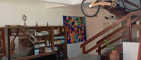 A spacious living area with a staircase, a wooden bookshelf, a colorful abstract painting, and a bicycle mounted on the wall.