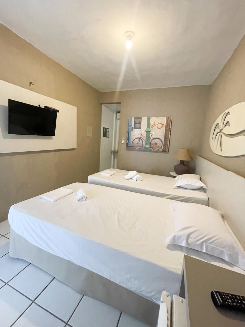 Quarto de hotel com uma cama grande, uma televisão na parede e um quadro de bicicletas.