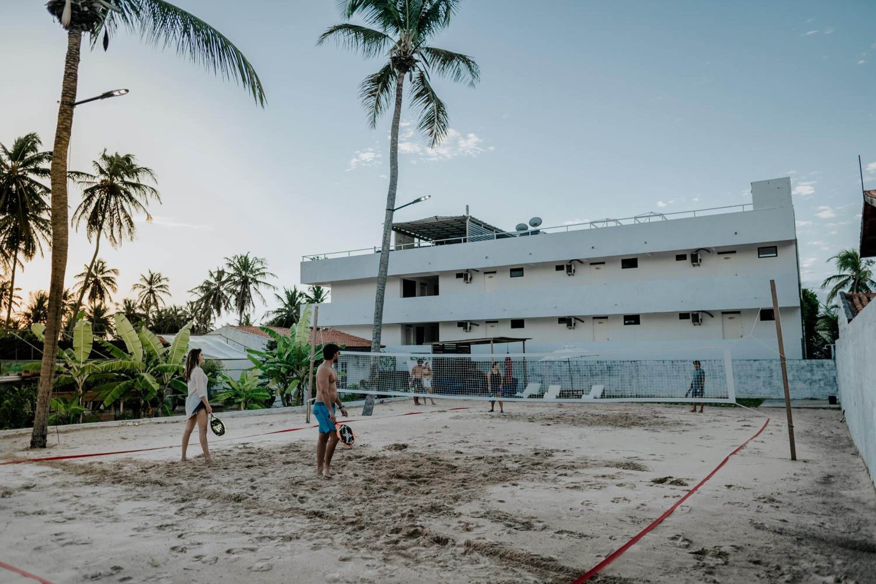 Una cancha de voleibol de playa con red, palmeras y un edificio al fondo.