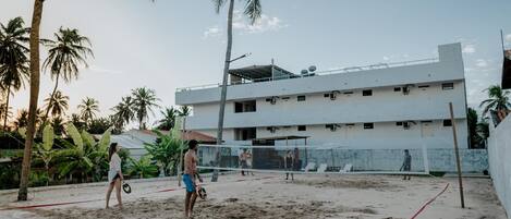 Una cancha de voleibol de playa con red, palmeras y un edificio al fondo.
