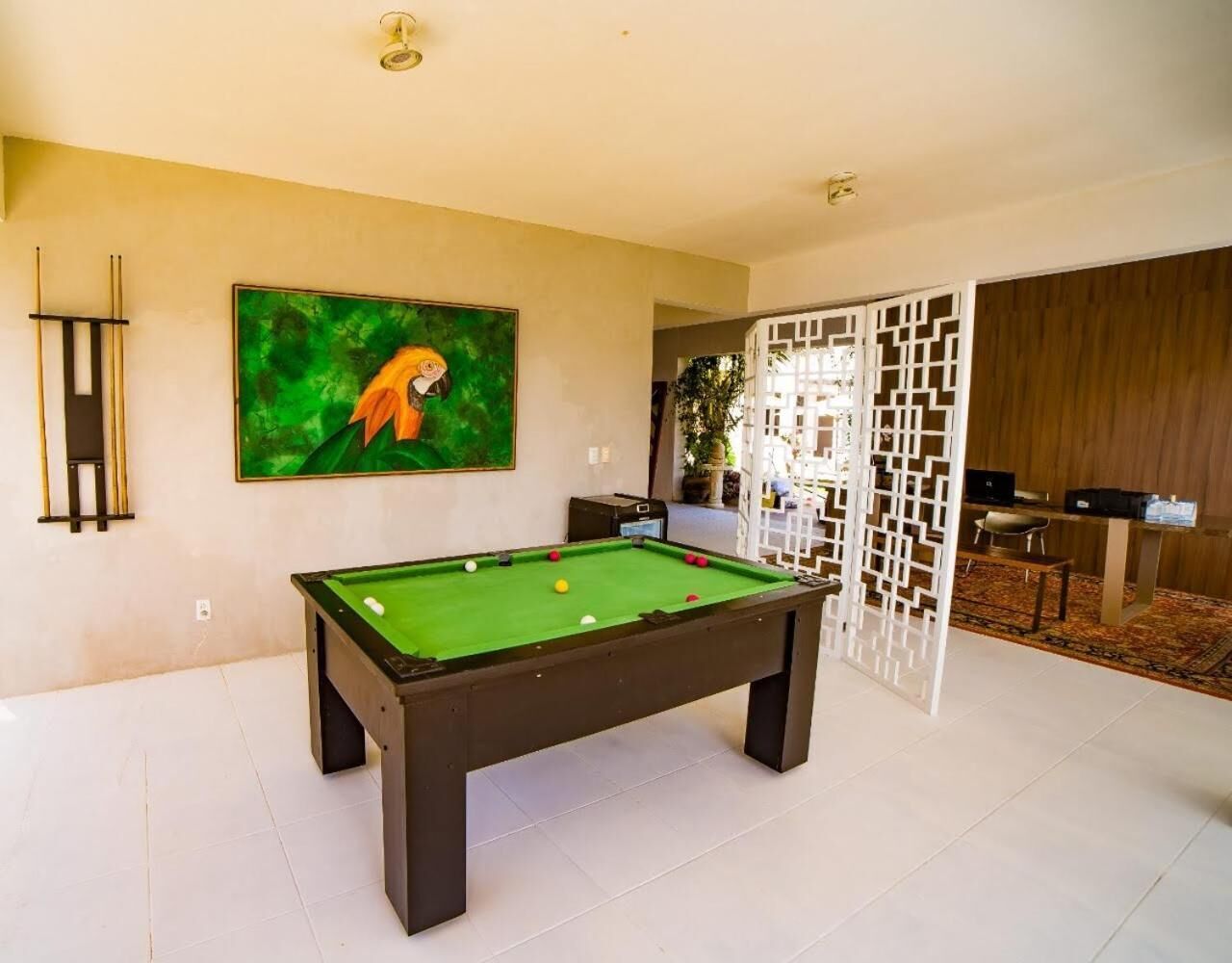 Een pooltafel in een moderne ruimte met een groen vilt oppervlak, een schilderij van een papegaai aan de muur, en een wit scheidingswand met een geometrisch patroon.