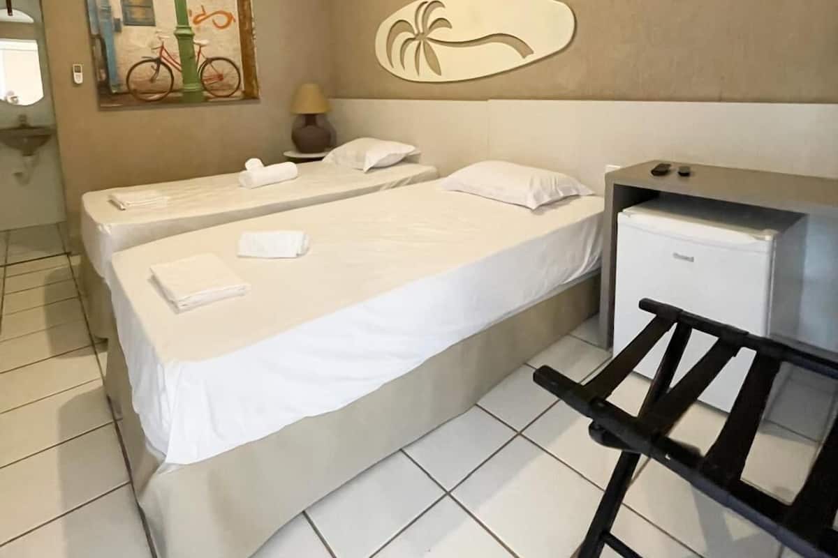 Une chambre d’hôtel avec deux lits, un petit réfrigérateur, une œuvre d’art accrochée au mur et un sol carrelé.