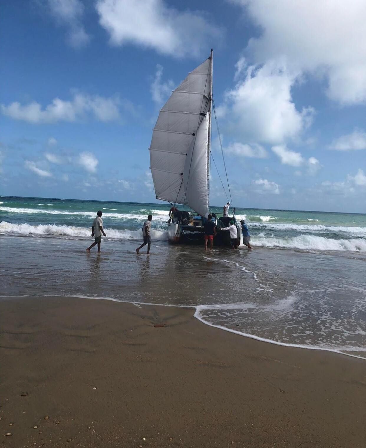 Un voilier sur une plage, avec des personnes qui se promènent autour.
