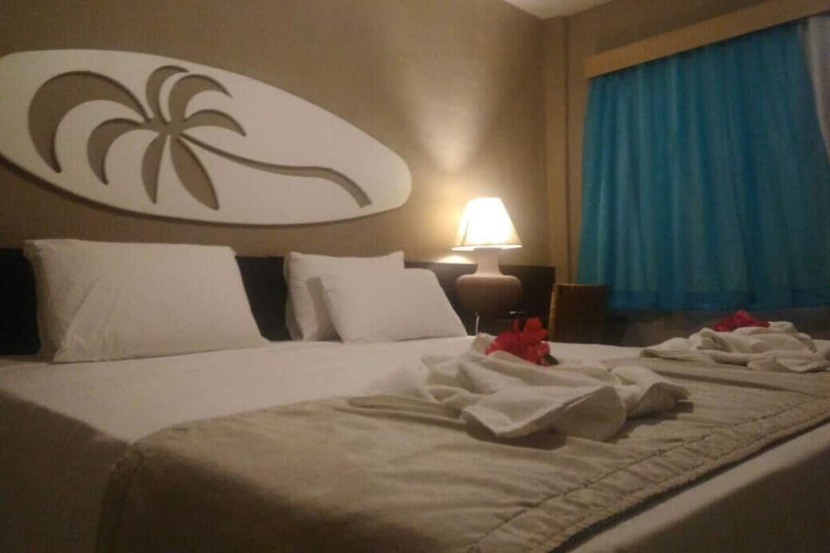 Une chambre d’hôtel avec un lit, une table de chevet, une lampe et une grande fenêtre avec des rideaux.
