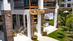 A modern hotel entrance with a wooden sign, outdoor seating, and potted plants. - Inn Tribus (Trairi)