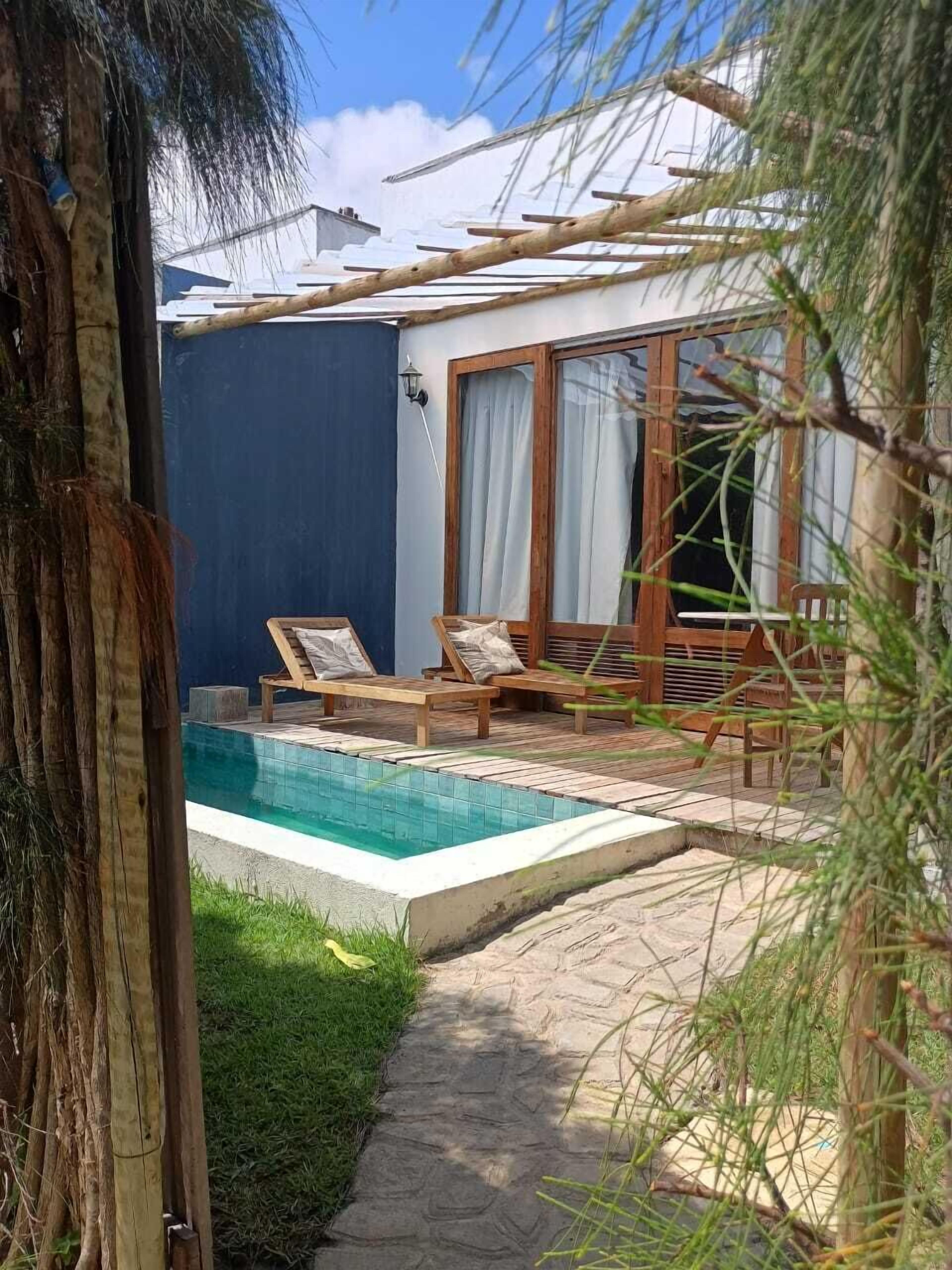 Una zona junto a la piscina con terraza de madera, sillas de descanso y una piscina pequeña.