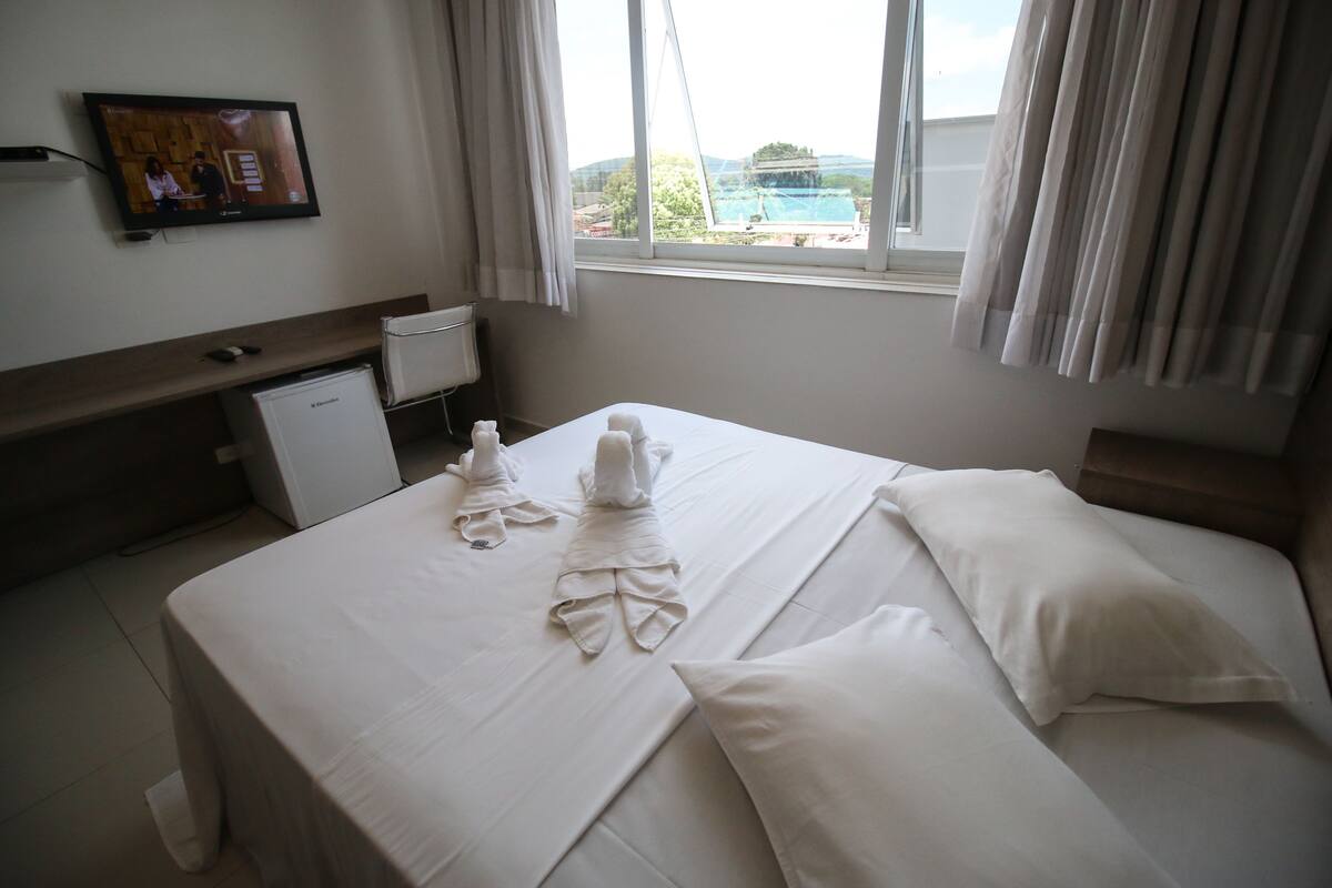 Une chambre d’hôtel avec un lit bien fait, un petit bureau et un téléviseur fixé au mur.