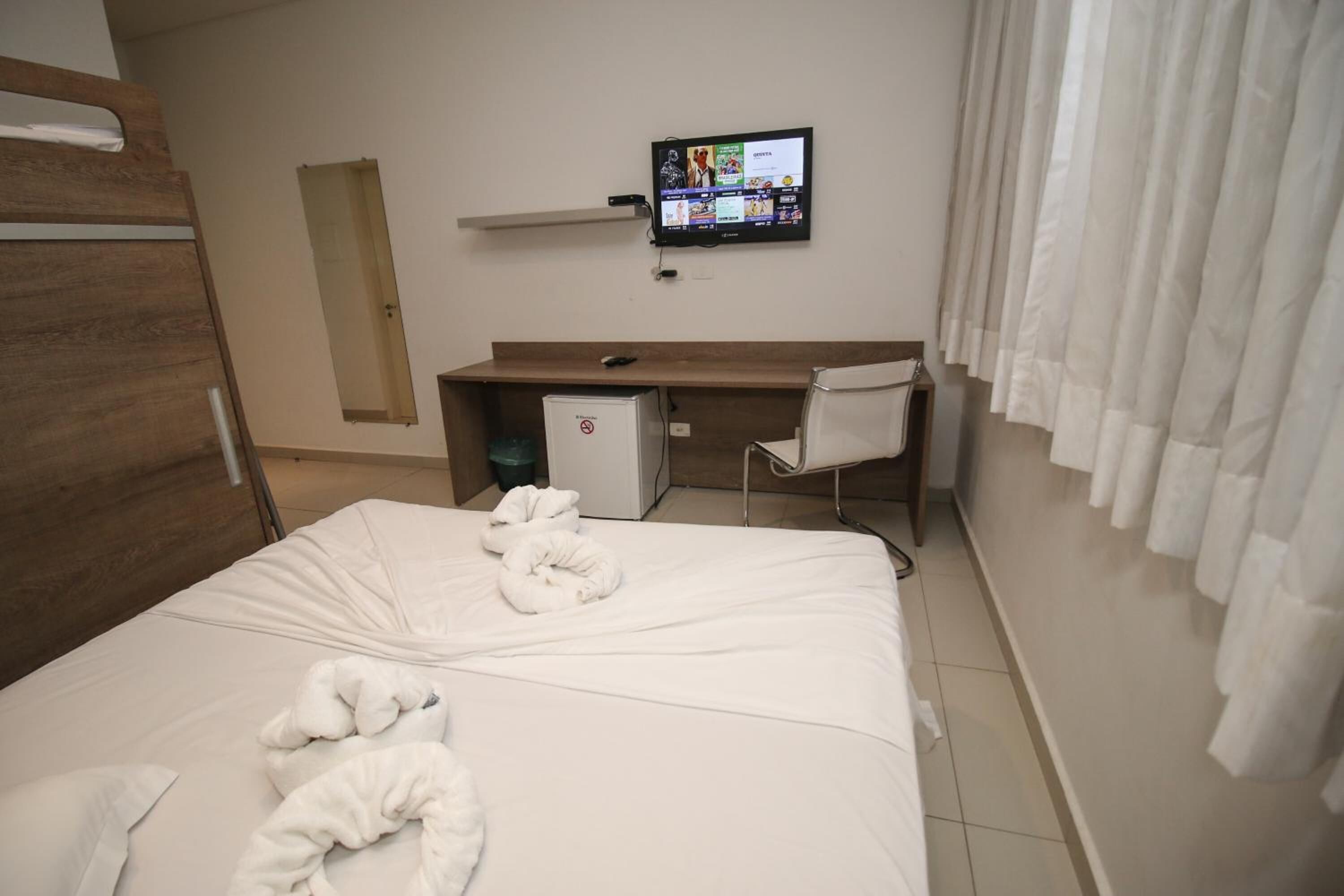 A hotel room with a bed, a desk, a television, and a shower area.