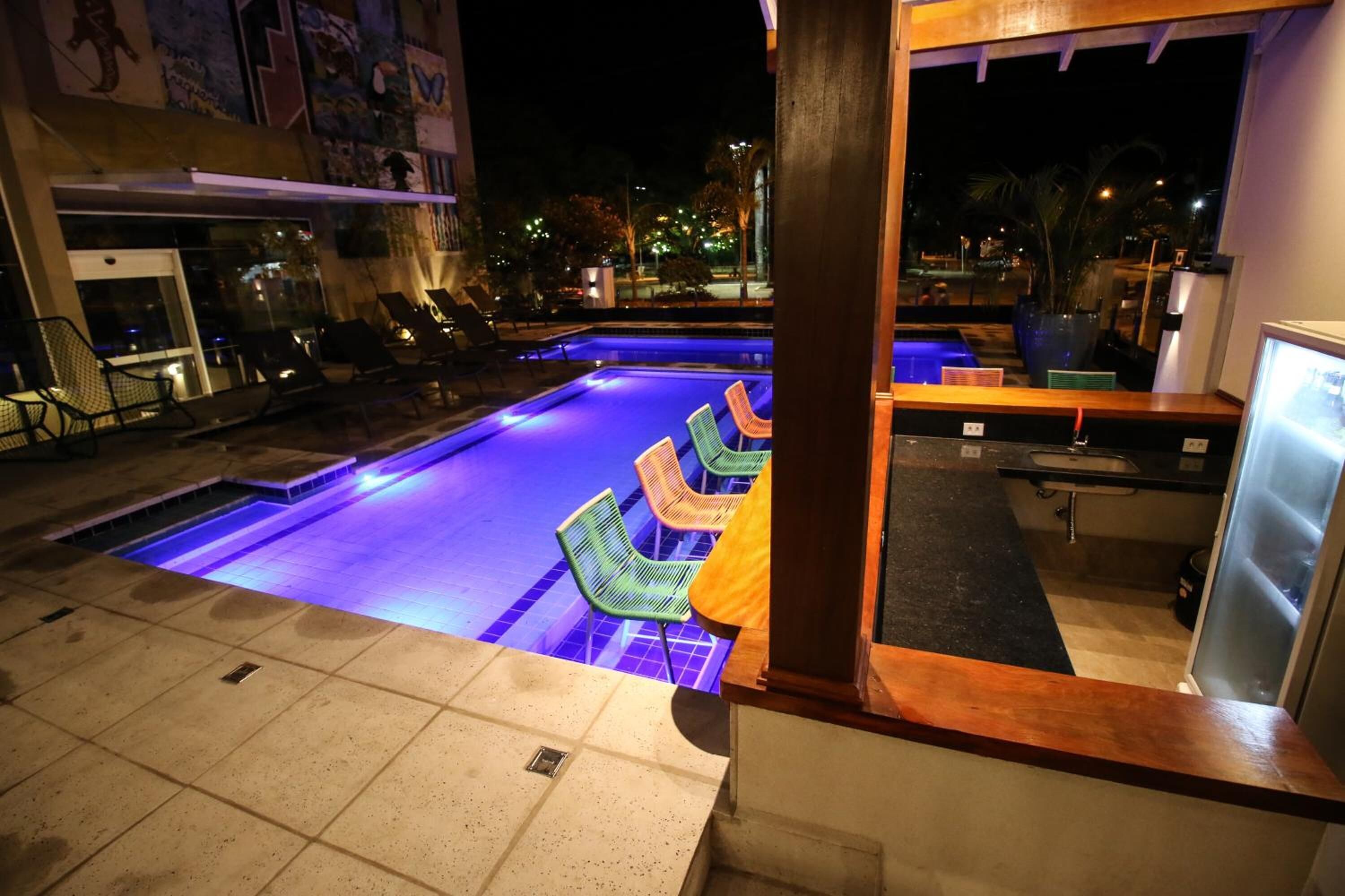Un espace piscine nocturne avec des chaises longues et un bar.