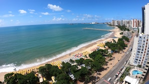 A beach with umbrellas and a road alongside a high-rise building. - Grupo Vip Landscape Fortaleza (Fortaleza)