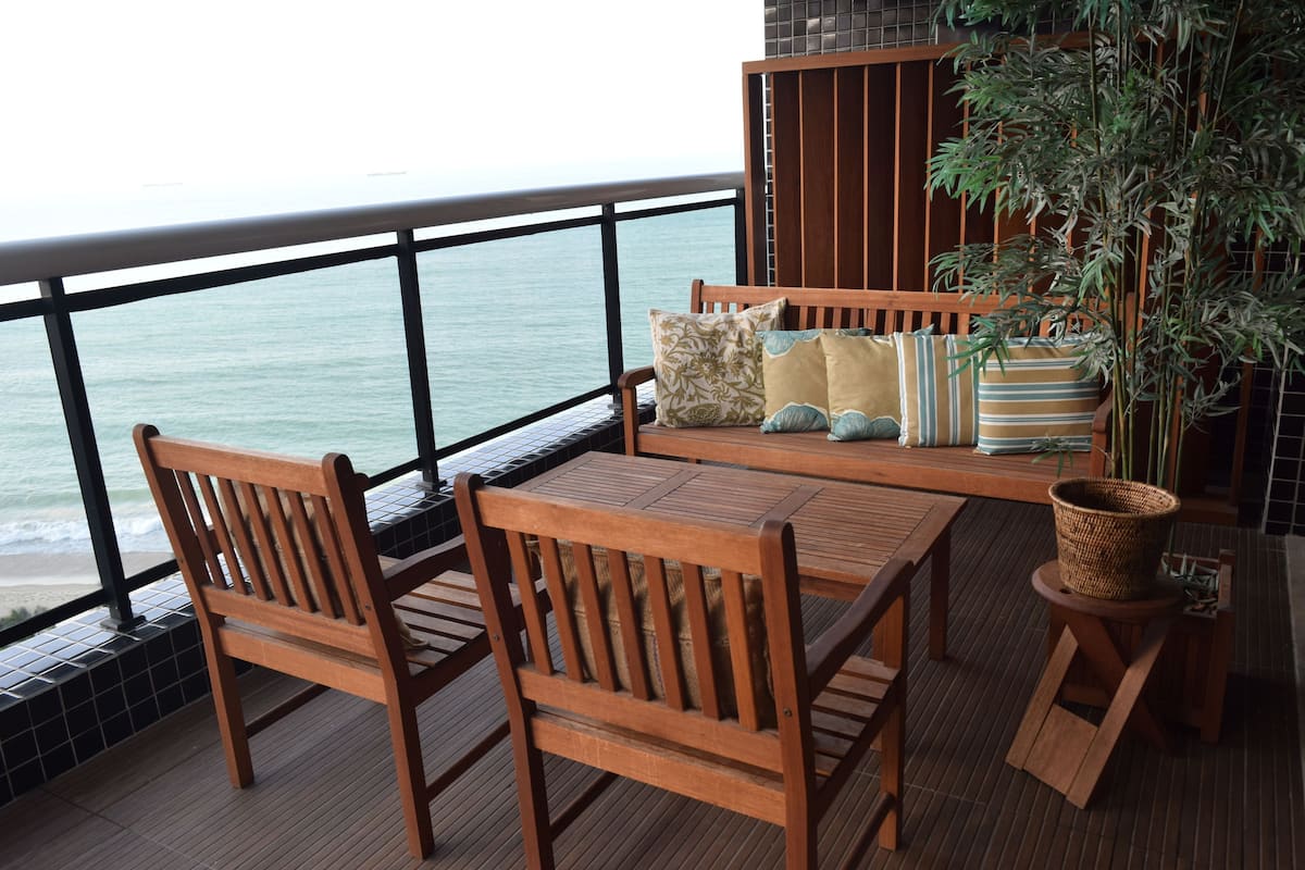 A wooden deck with a table and chairs, overlooking the sea.