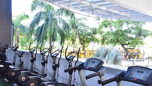 A row of stationary bikes with a view of palm trees and a covered area. - Grupo Vip Landscape Fortaleza (Fortaleza)