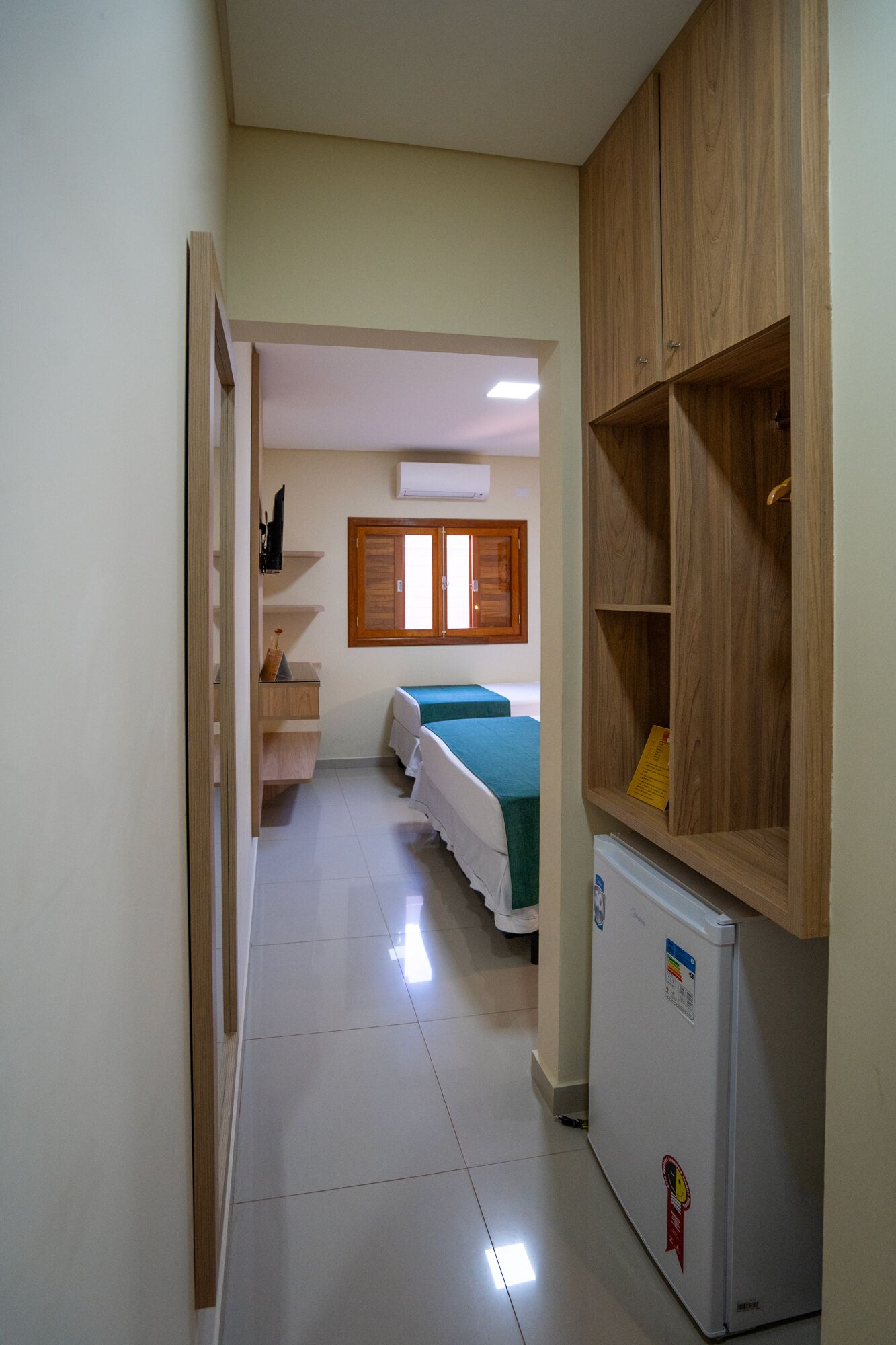 Un couloir étroit mène à une chambre dotée de deux lits, d’une armoire en bois et d’un petit réfrigérateur.