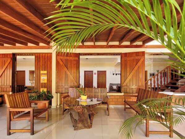 A spacious lobby with a wooden ceiling, a central glass-top coffee table surrounded by chairs, and a staircase leading to an upper level.