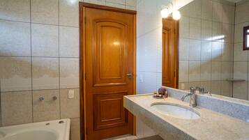 A bathroom with a wooden door, a bathtub, a sink with a mirror, and tiled walls.